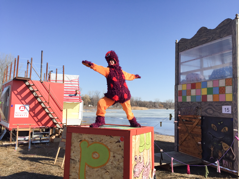 a woman dressed in a purple fuzzy costume stands on top of a colorful wooden block