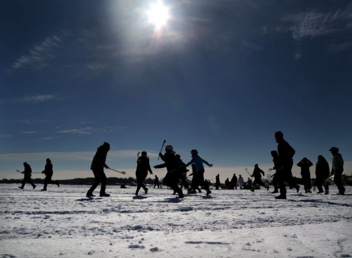 people playing lacrosse on snow-covered lake on a sunny day