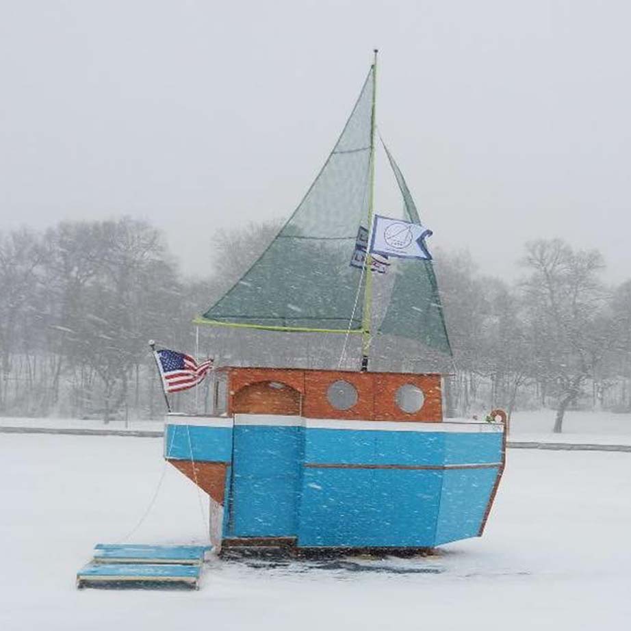 photo of a sail boat shanty in the snow on a frozen lake