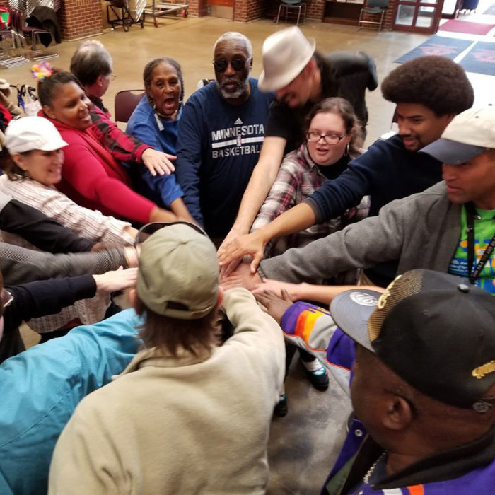 a group of people in a circle reach towards the center with one hand each.