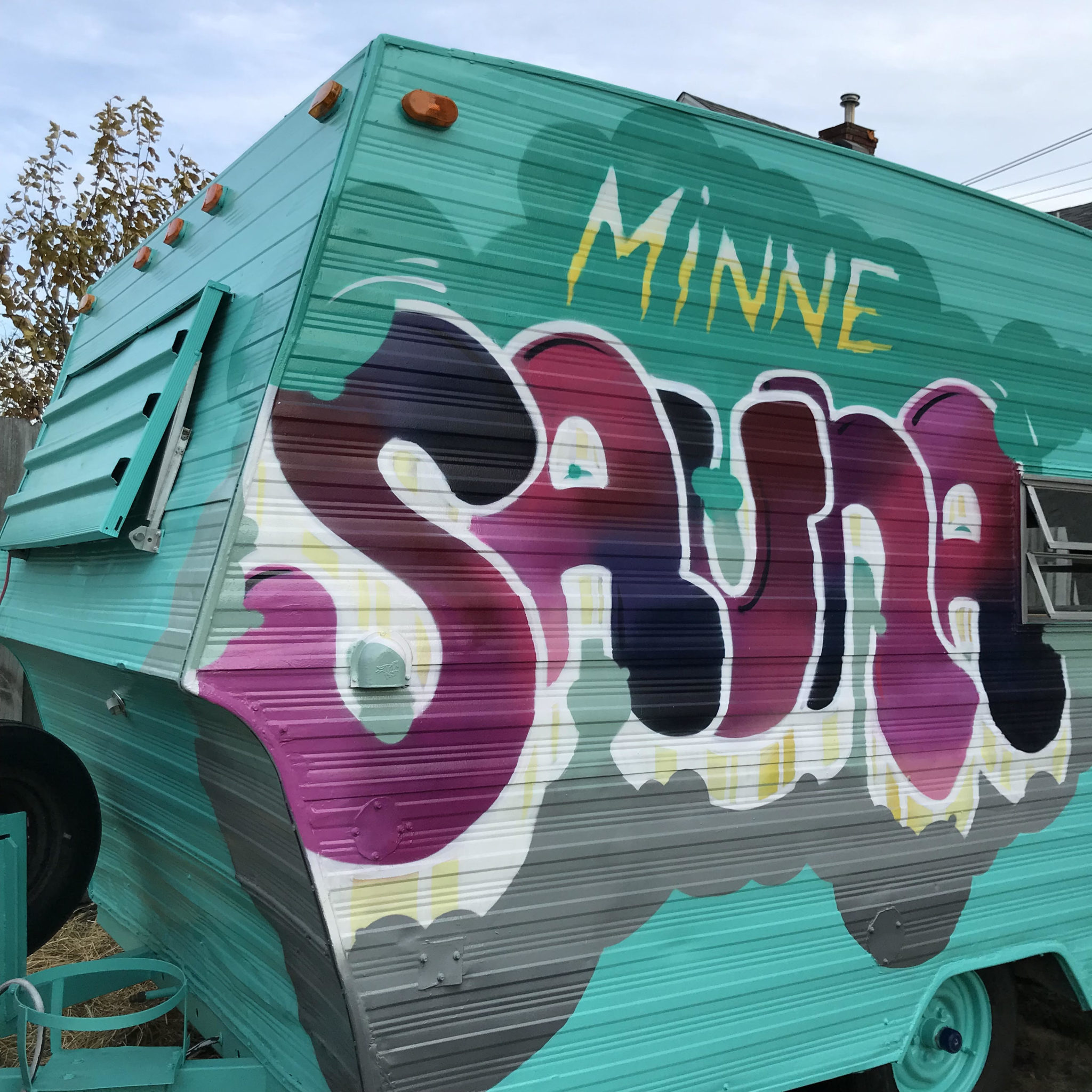 Close up teal camper van labeled "Minne Sauna" in huge bubbly letters painted grapey purple colors.