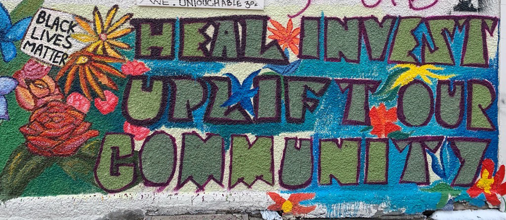 colorful painted mural on a wall with flowers and text reading: 'heal, invest, uplift our community'