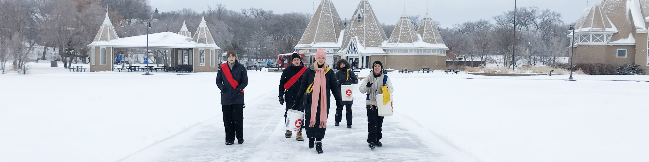 A few purposeful looking volunteers, some wearing red sashes, approach the camera with the Bde Unma Bandshell behind them.