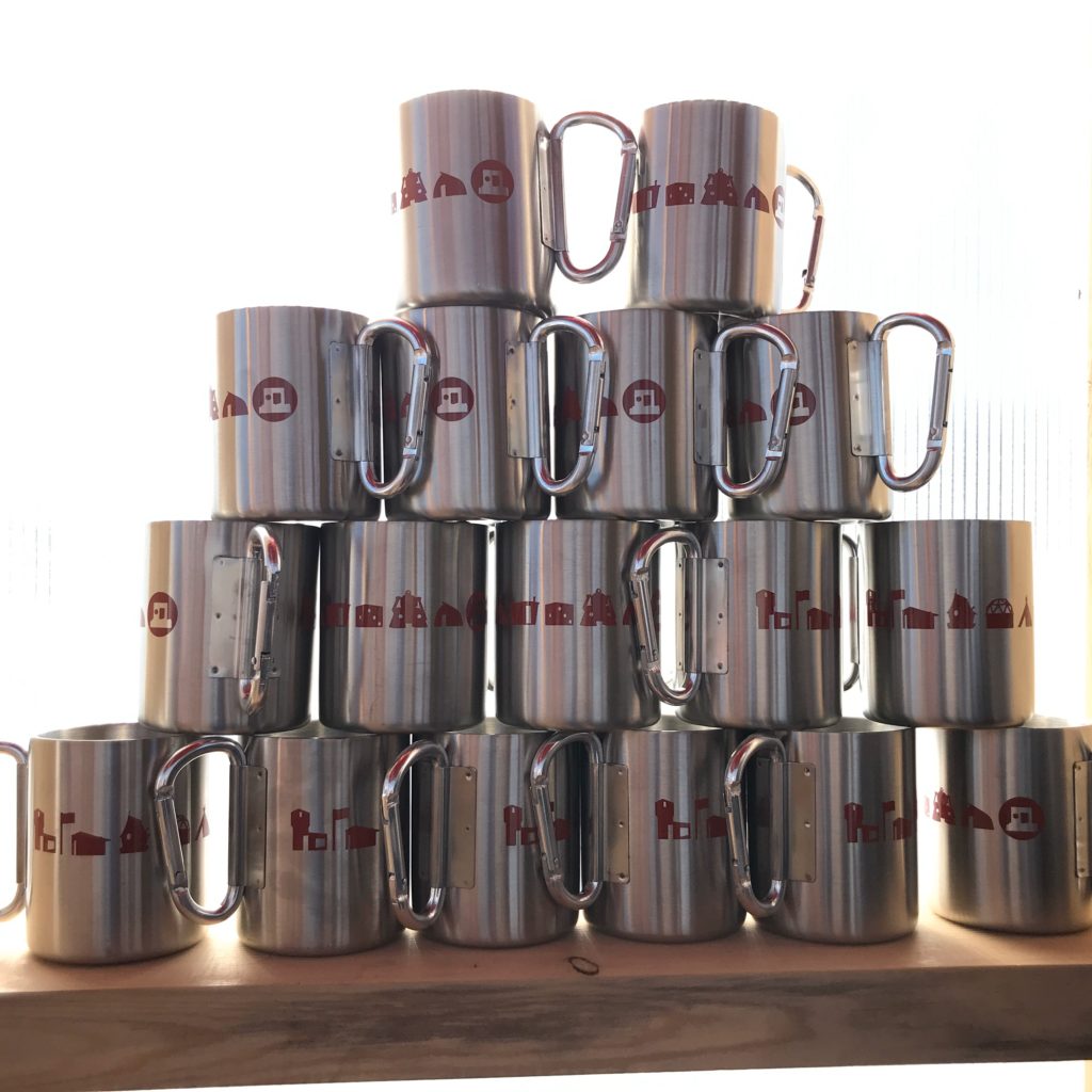 A pyramid arrangement of shiny silver camp mugs with red art shanty graphics on them