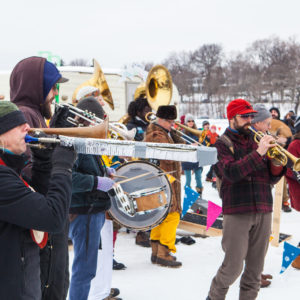 A brass band plays their horns amidst a colorful village on a frozen lake.
