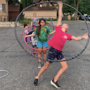 A line of kids play with hula hoops on pavement