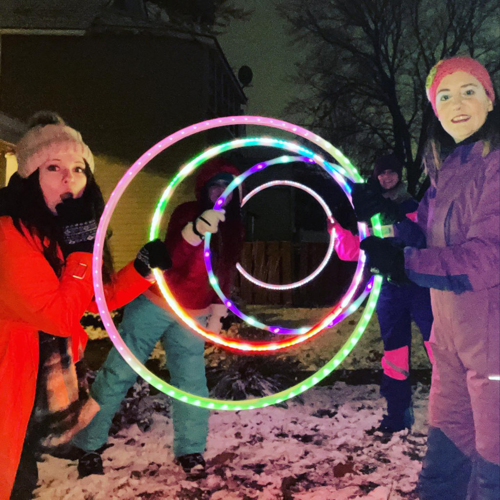 three people i snowsuits pose with glowing hula hoops at dusk