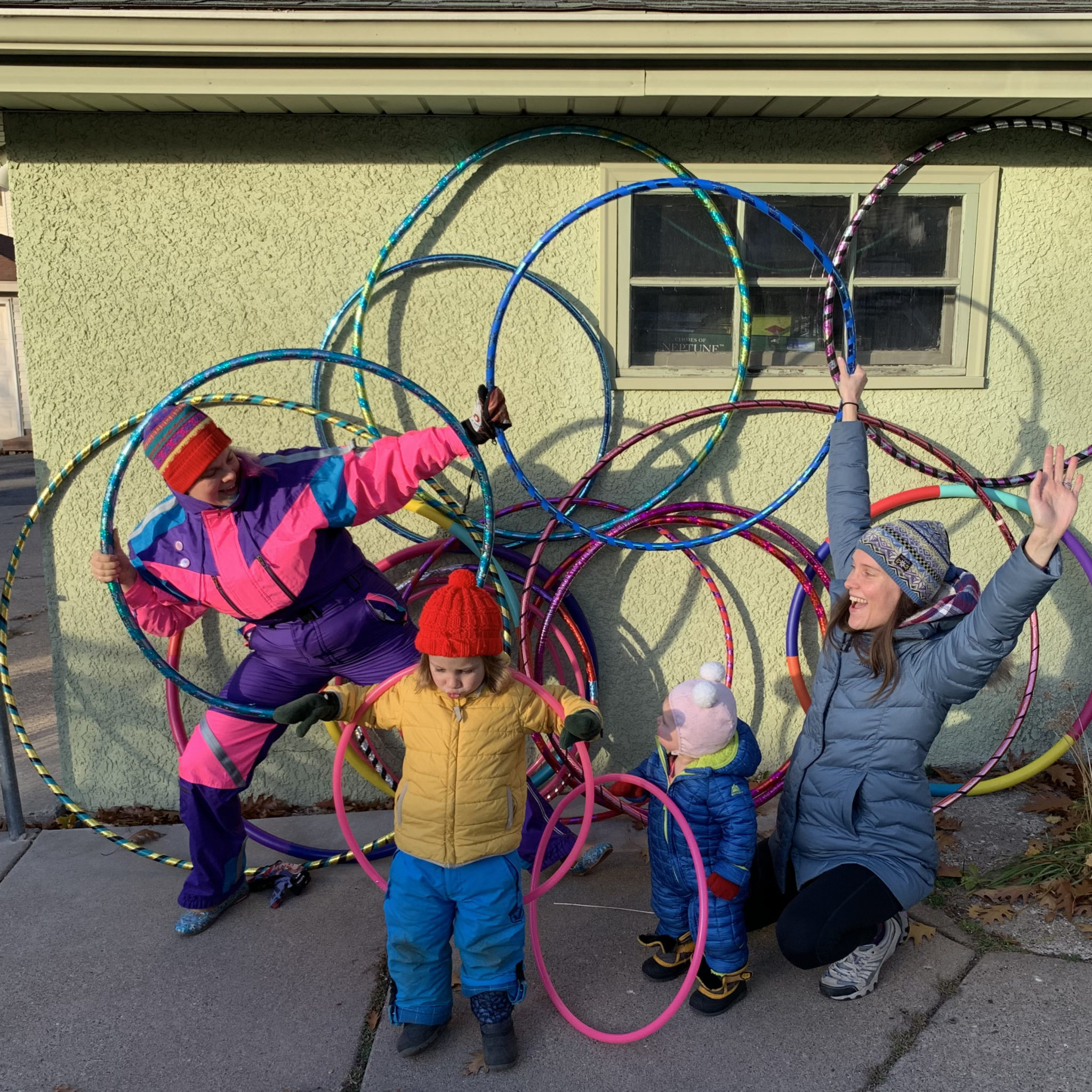two adults and a kid, all in snowsuits, pose with a dozen hula hoops