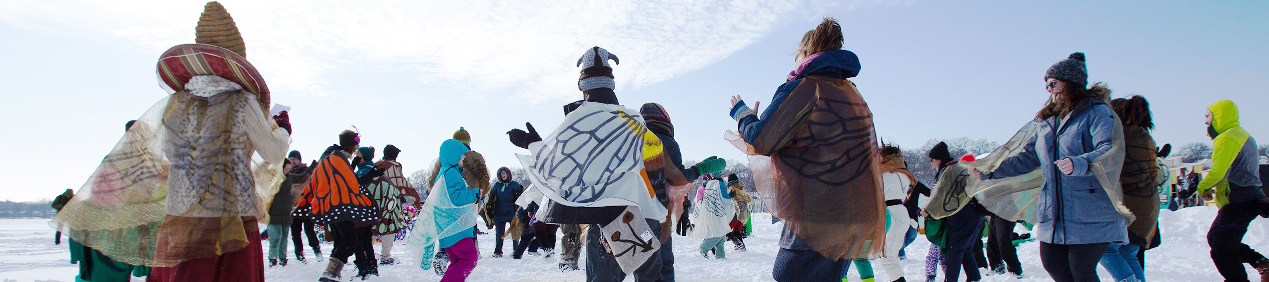 A crowd of people dance around in butterfly wings on a snow-covered lake