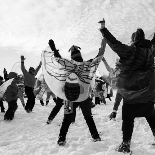 A black and white image of adults in insect costumes dancing on the snow