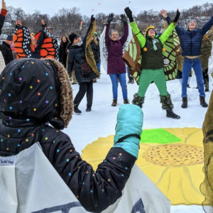 A photo of people wearing colorful insect costumes dancing on a frozen lake