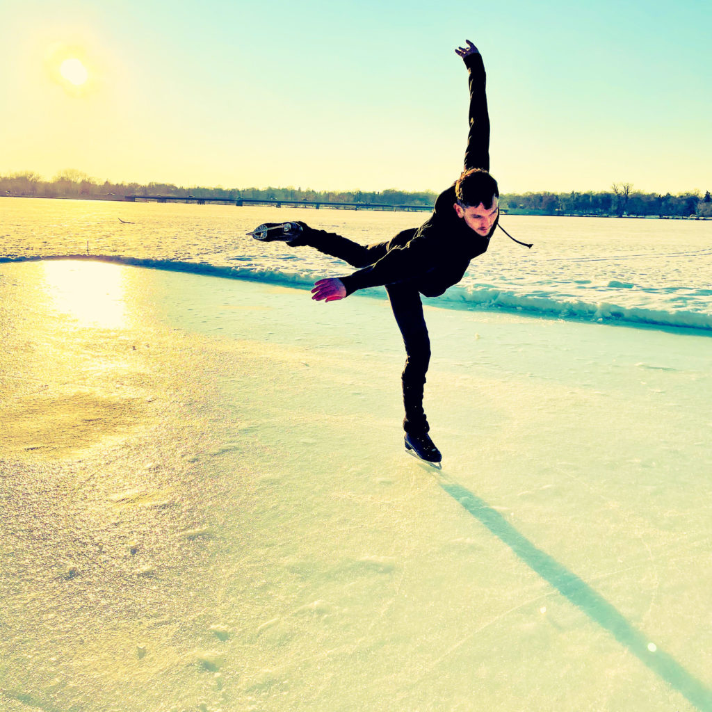 A skater glides across the frozen lake on one leg with arms outstretched at sunset.