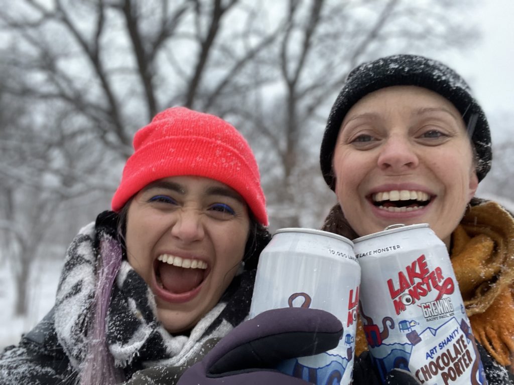 two people clink their cans while laughing in the falling snow