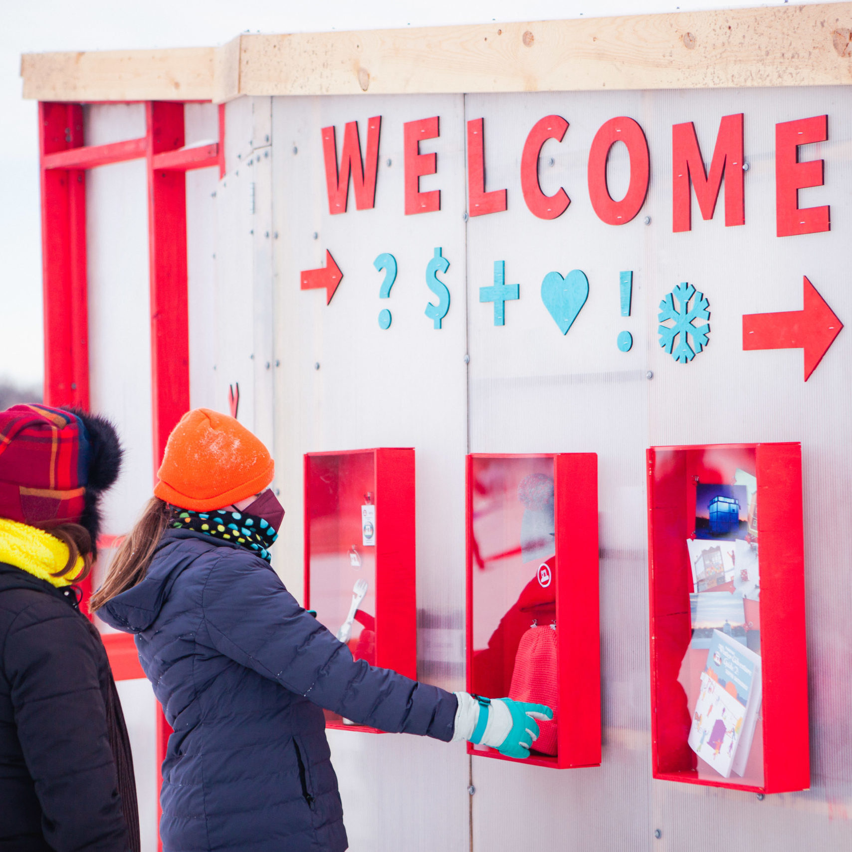 two people look at boxes containing merchandise. "Welcome" is spelled out in giant red letters.