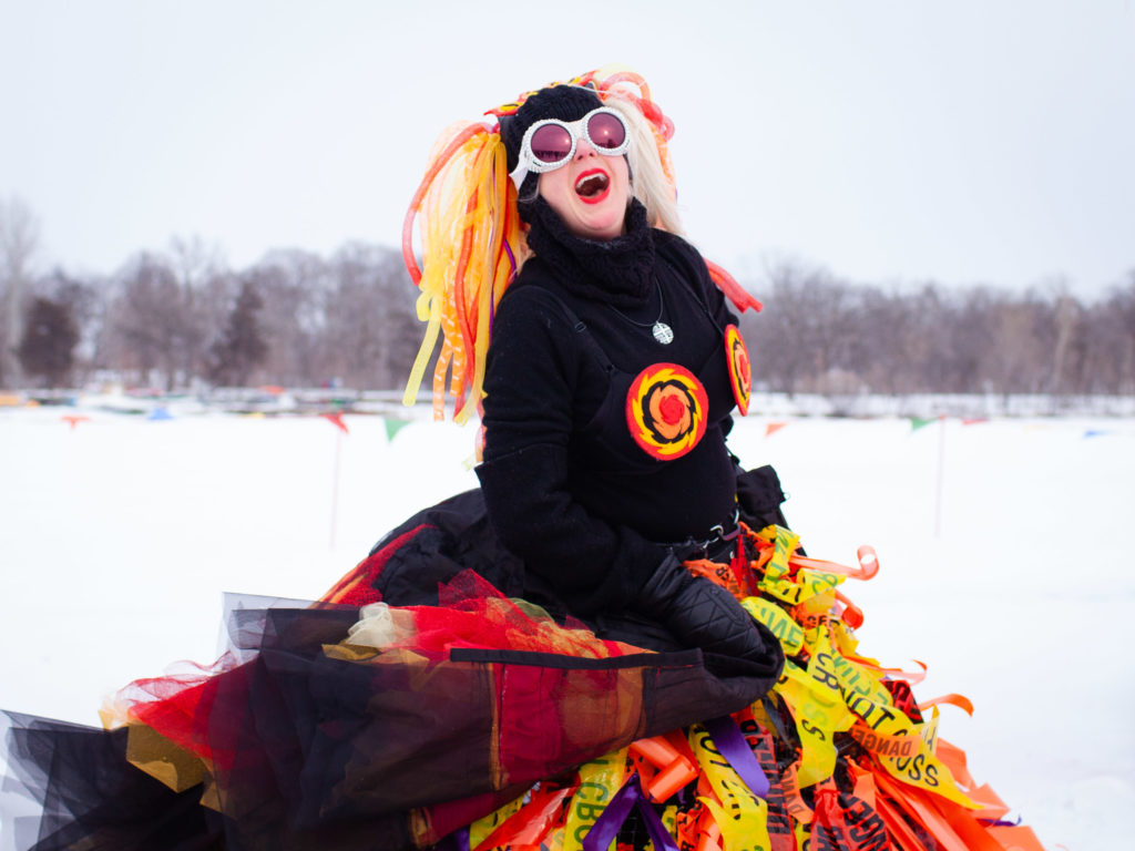A person wearing an elaborate fire costume laughs as she struts by