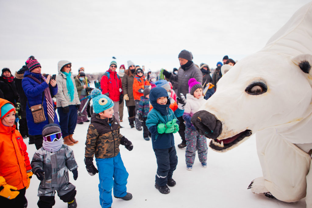 A group of bundled up kiddos look in awe at a giant polar bear puppet