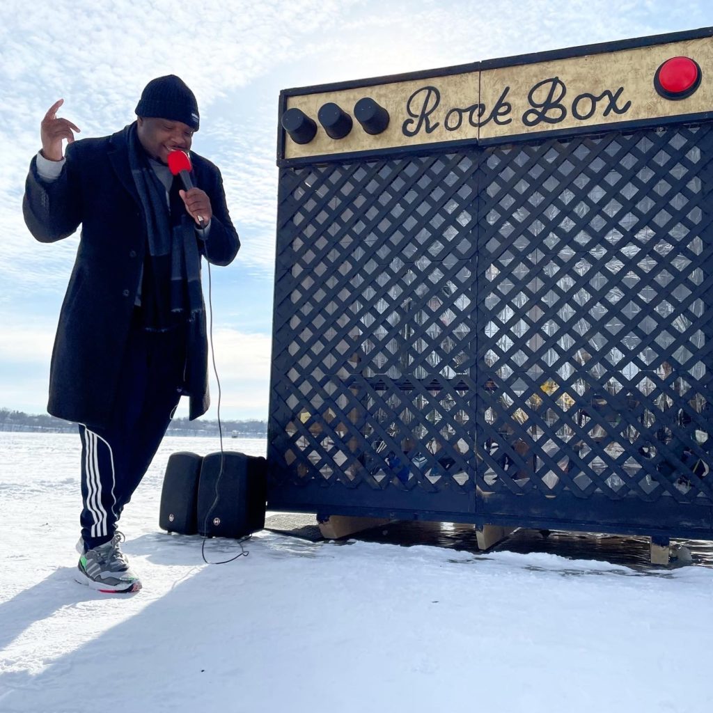 A person sings into a mic in front of an amp-shaped shanty.