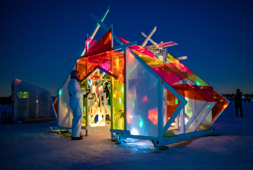 lights glow inside a shanty, illuminating neon colors against a deep blue sky