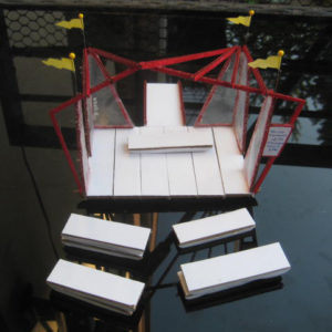 a front view of a stage model. It has red beams, a white platform and benches, and yellow flage.