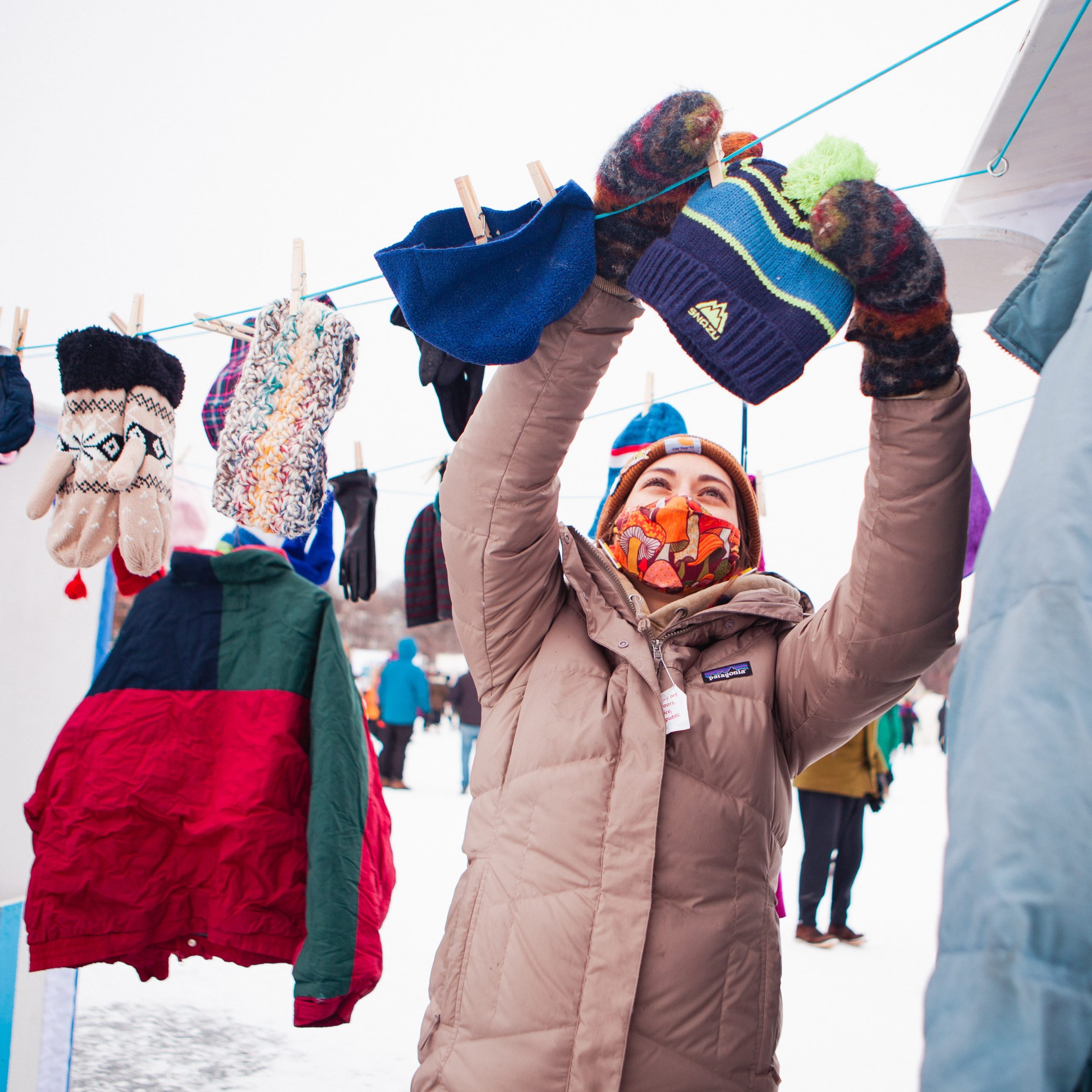 A bundled up person hangs a hat on a clothesline full of winterwear outside.