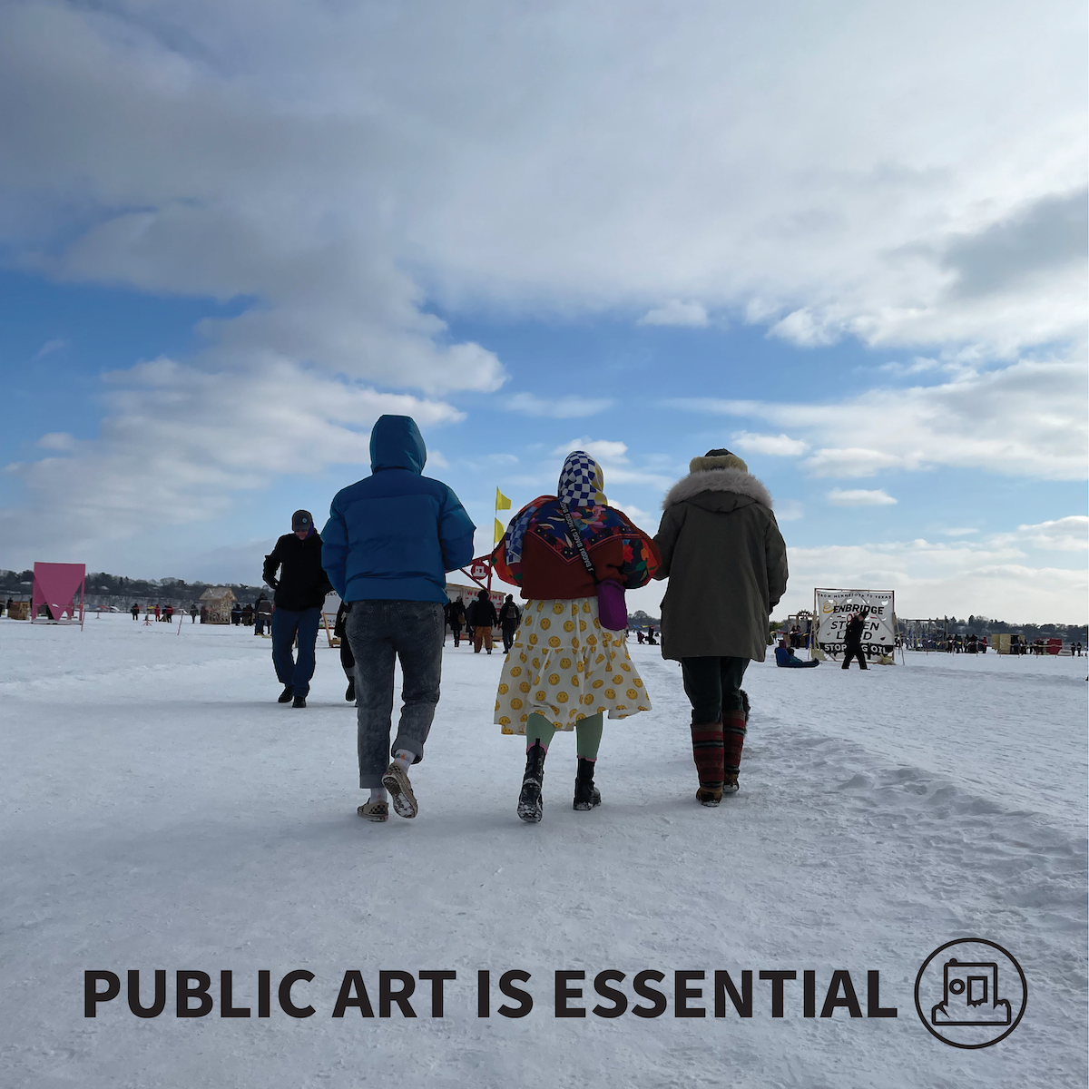 three people walk across a snowy frozen lake towards a shanty village on a blue-sky puffy-cloud day. Black text reads 'public art is essential' next to an outline of the art shanty logo