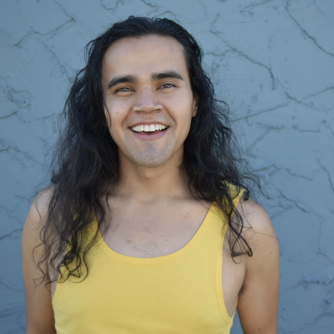 a person wearing a yellow tank top smiles while posing in front of a blue wall