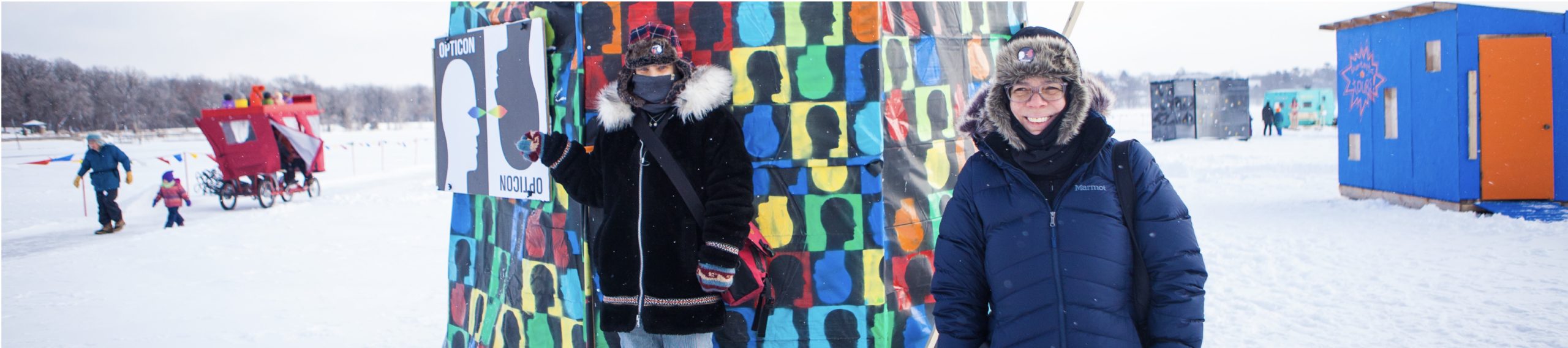 Two bundled up people greet the camera at their colorful yurt shanty