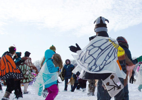 Art shanty Pollinator dancers dressed like insects dance in a cirle on the ice.
