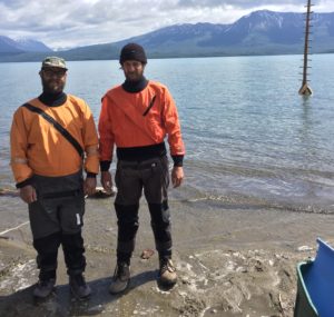 Two people wearing bizarre orange and black uniforms stand in front of a body of water