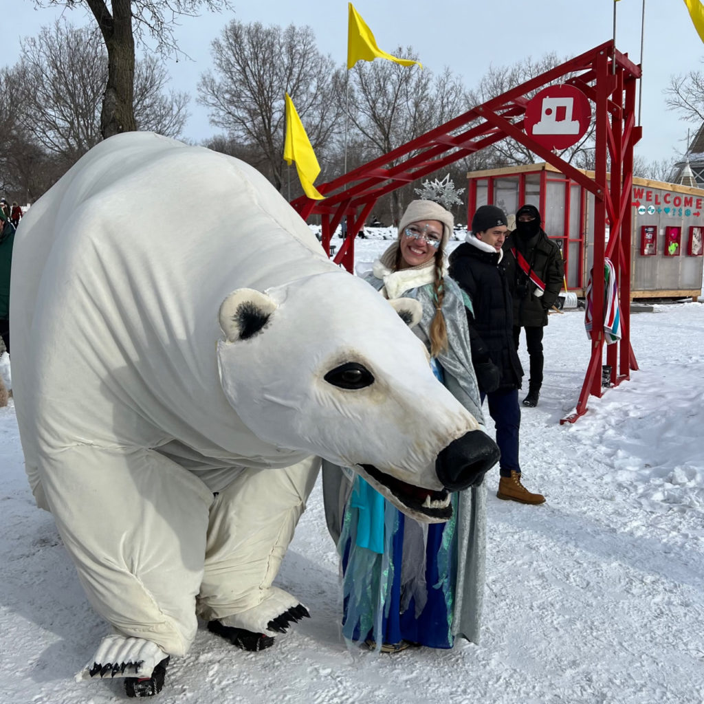 A life sized polar bear puppet smiles next to a person in an icy blue costume