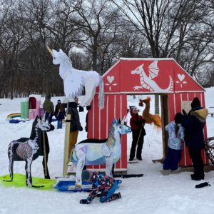 Activity of magical creatures - including a skeleton unicorn - surround a red barn shaped shanty