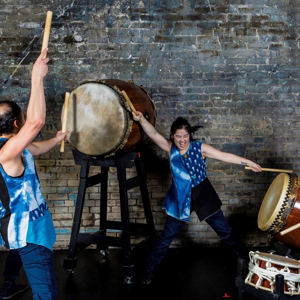 two people wearing blue costumes play taiko drums