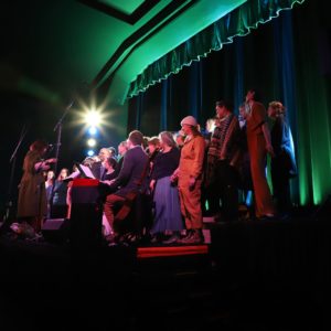 A choir sings in a a dark room lit in green and purple
