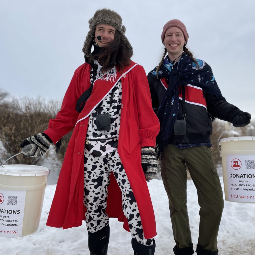 Two smiling people in fantastic outfits hold donation buckets