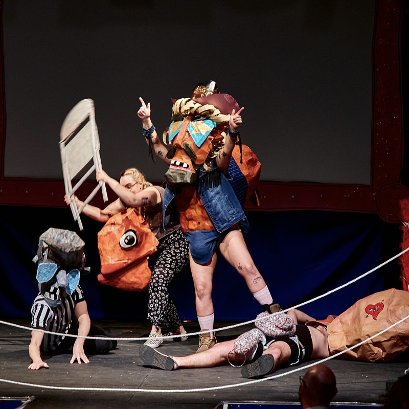 A group of people in tight costumes and giant puppet masks wrestle