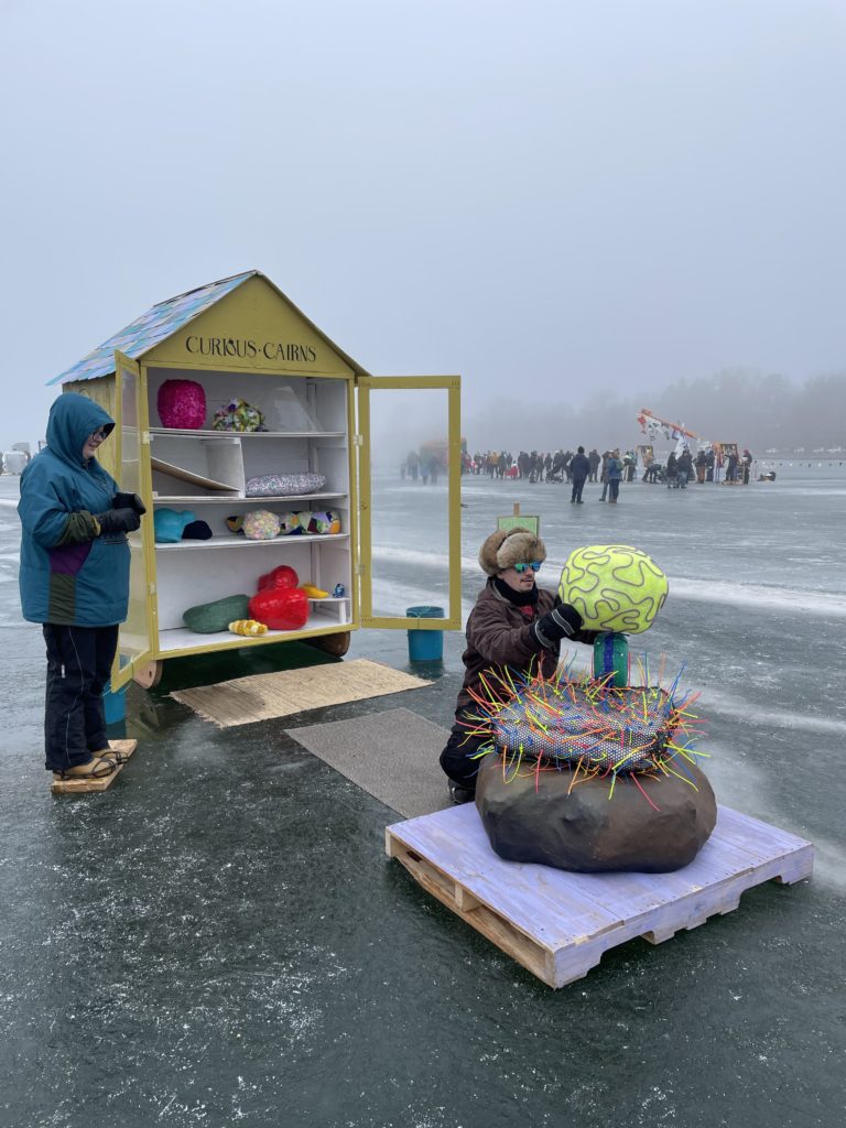a person stacks art rocks while people are in the distance on the frozen lake