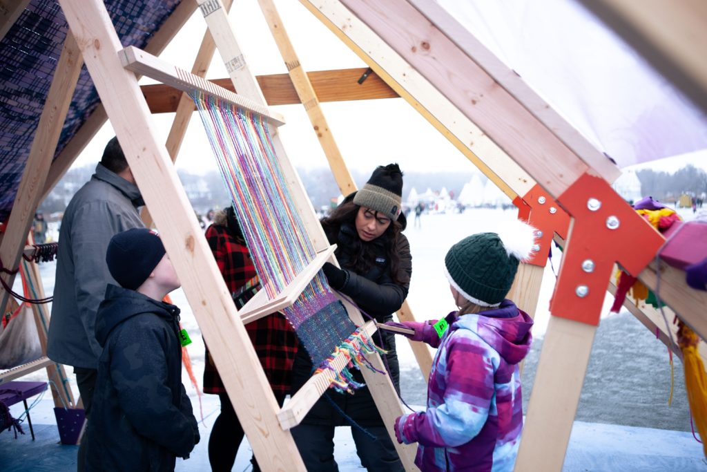 An artist helps people weave on a shanty that is in itself a giant loom