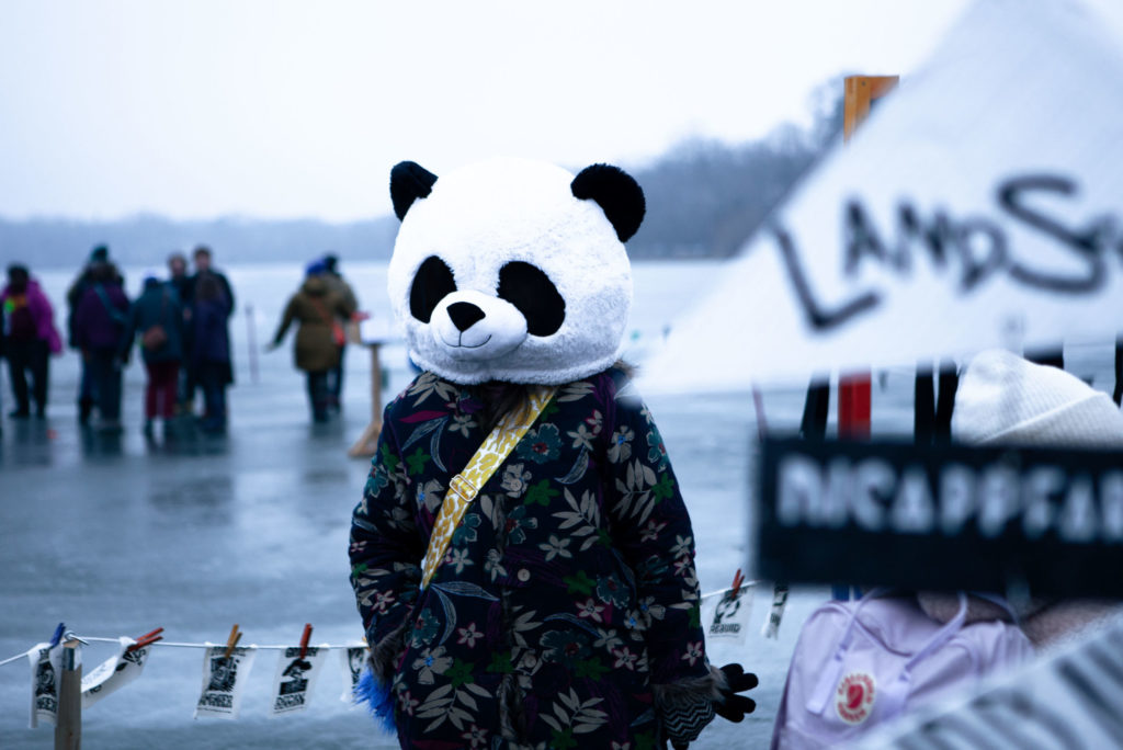 A person in a panda bear costume stands in the shanty village
