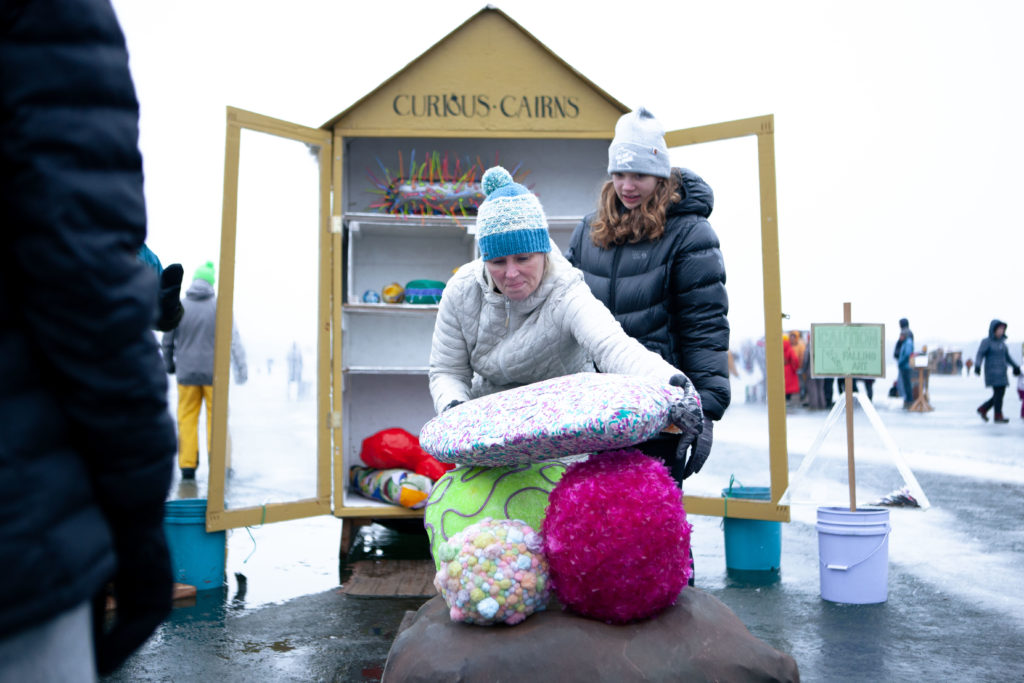 visitors stack giant colorful art rocks at an opened cabinet shanty