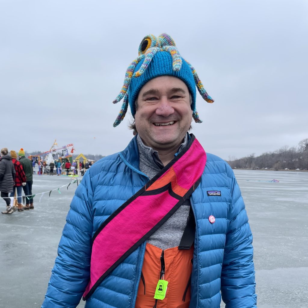 Darren smiles big while wearing his knit octopus hat and magenta art shanty sash