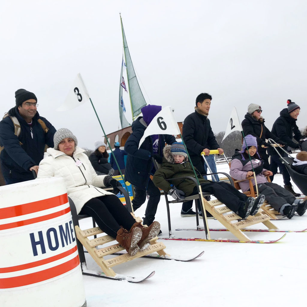 A group of people line up with kicksleds for a race on a frozen lake