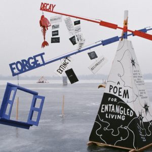 A black and white pyramid base supports giant mobile arms with words and objects hanging from them.