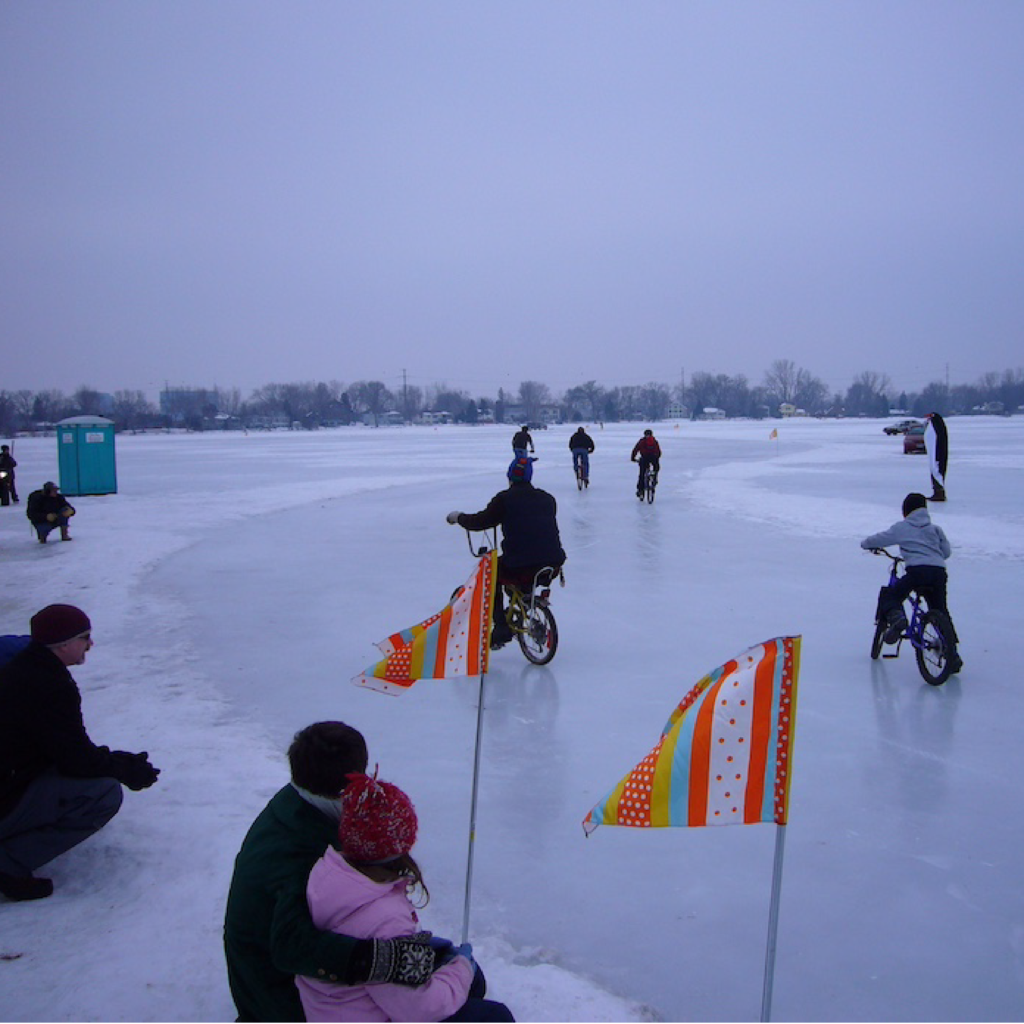 Orange and white striped flags mark a racing path on a frozen lake! Bicycles whiz by.