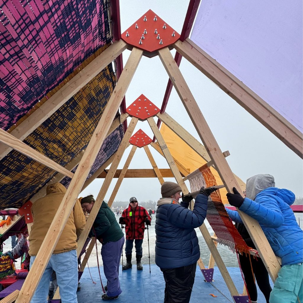 A photo from the inside of an A-frame shanty. People are actively weaving the walls.