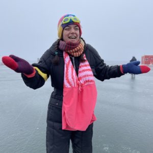 a person wears a pink swimsuit over a snowsuit on the frozen lake.