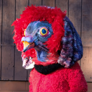 A blue pigeon mask on a performer wearing a fancy red outfit