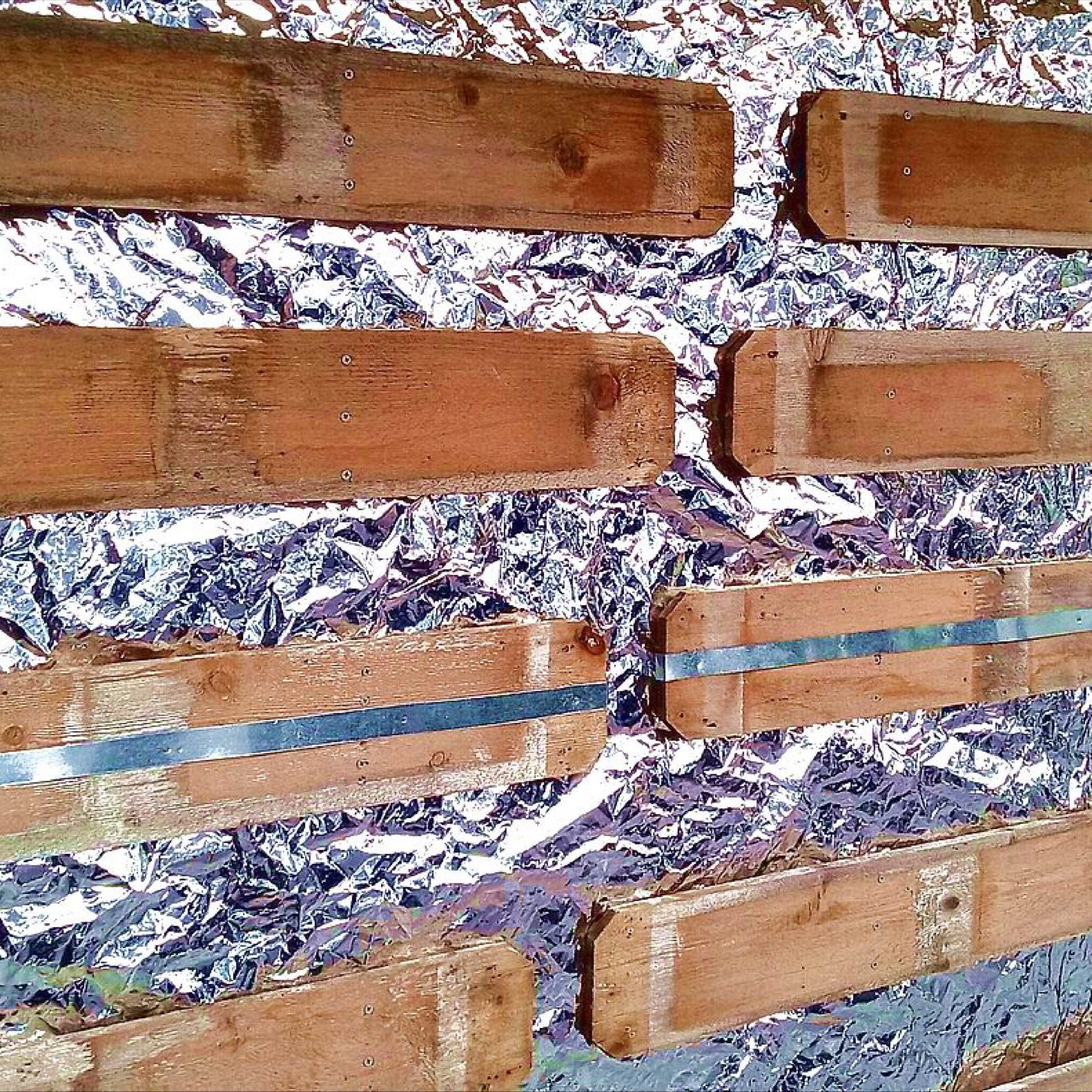 A closeup of a shanty wall from an angle - it includes wooden plants in a design overtop a crinkly shiny surface