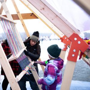 Two people work together to weave the wall of a shanty.