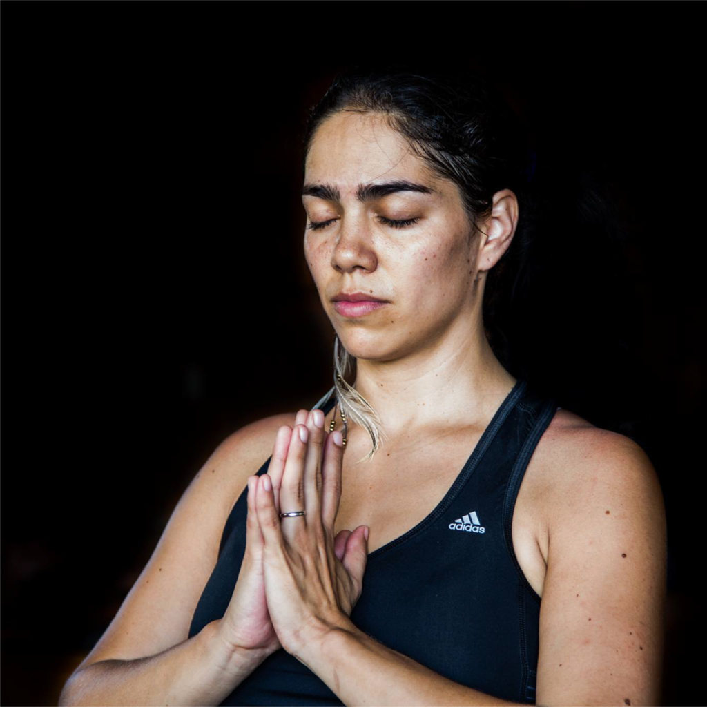 a headshot of a person in prayer pose against a black background