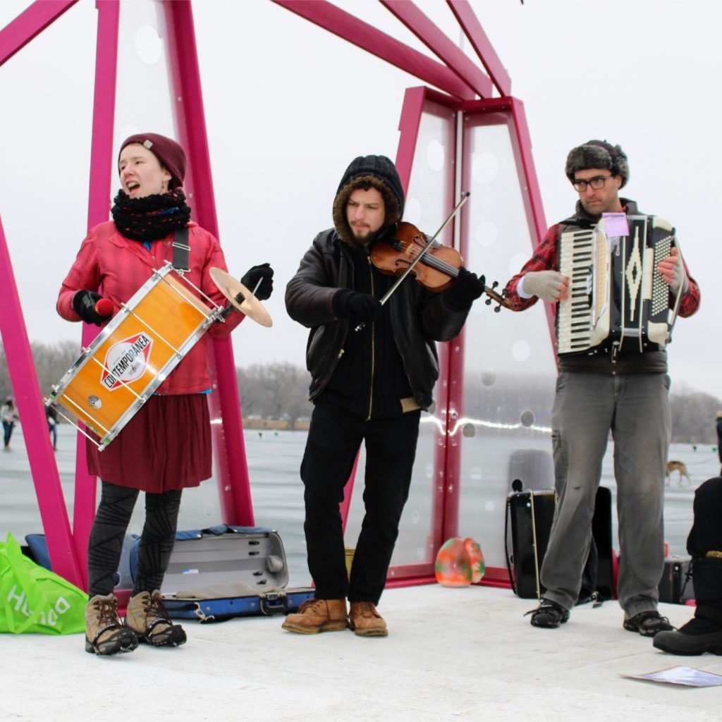 Three people playing a drum, violin and accordian on the shanty performance stage.